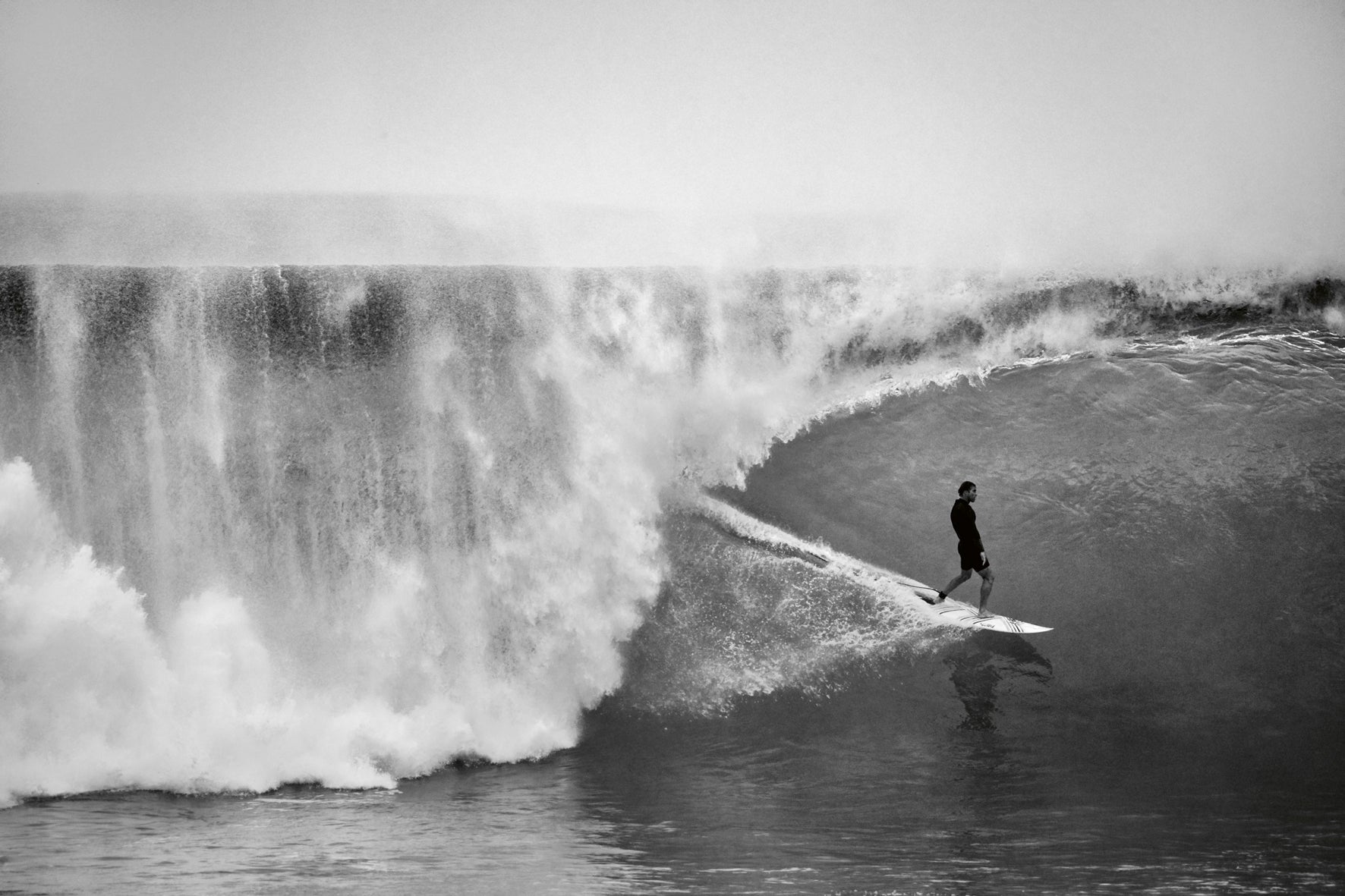 Person surfing a large wave in black and white.