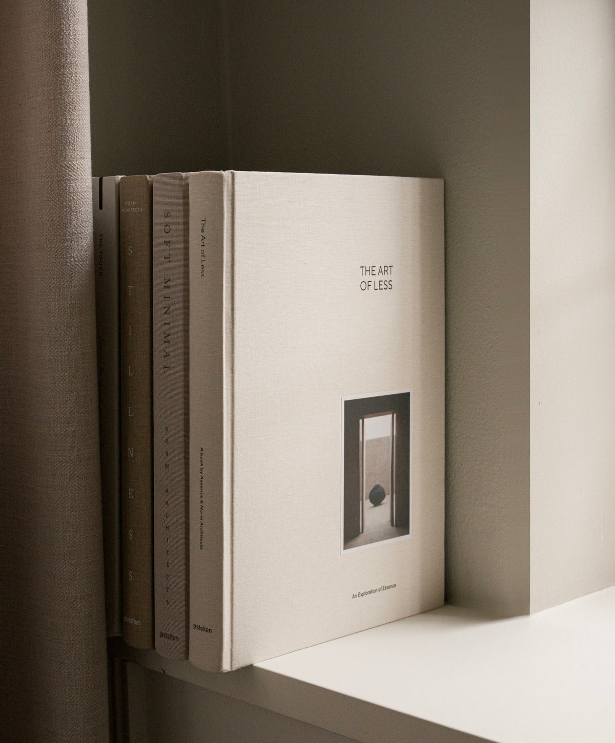 A stack of four art books on a white shelf, with the front book titled 'THE ART OF LEIS' by Heatherwick & Partners. The books have a warm off-white cover with black text and a minimalist architectural illustration.