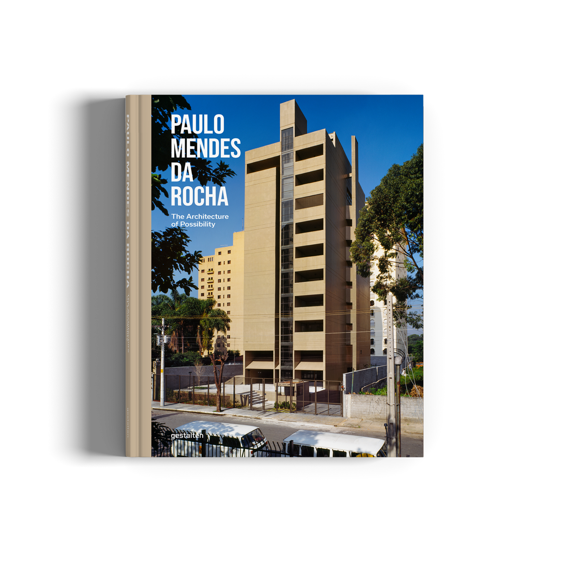 A hardcover book titled 'PAULO MENDES DA ROCHA: The Architecture of Possibility' is shown standing upright against a white background. The cover features a photograph of a mid-century modern apartment building under a blue sky, with a large blue title block on the left side.