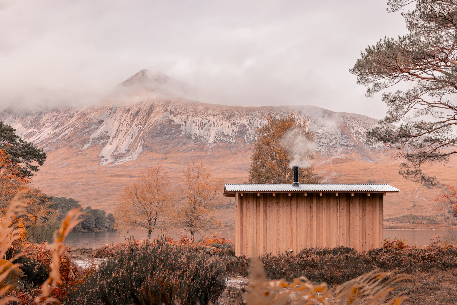 Wooden cabin in a mountainous landscape with trees and misty mountains.