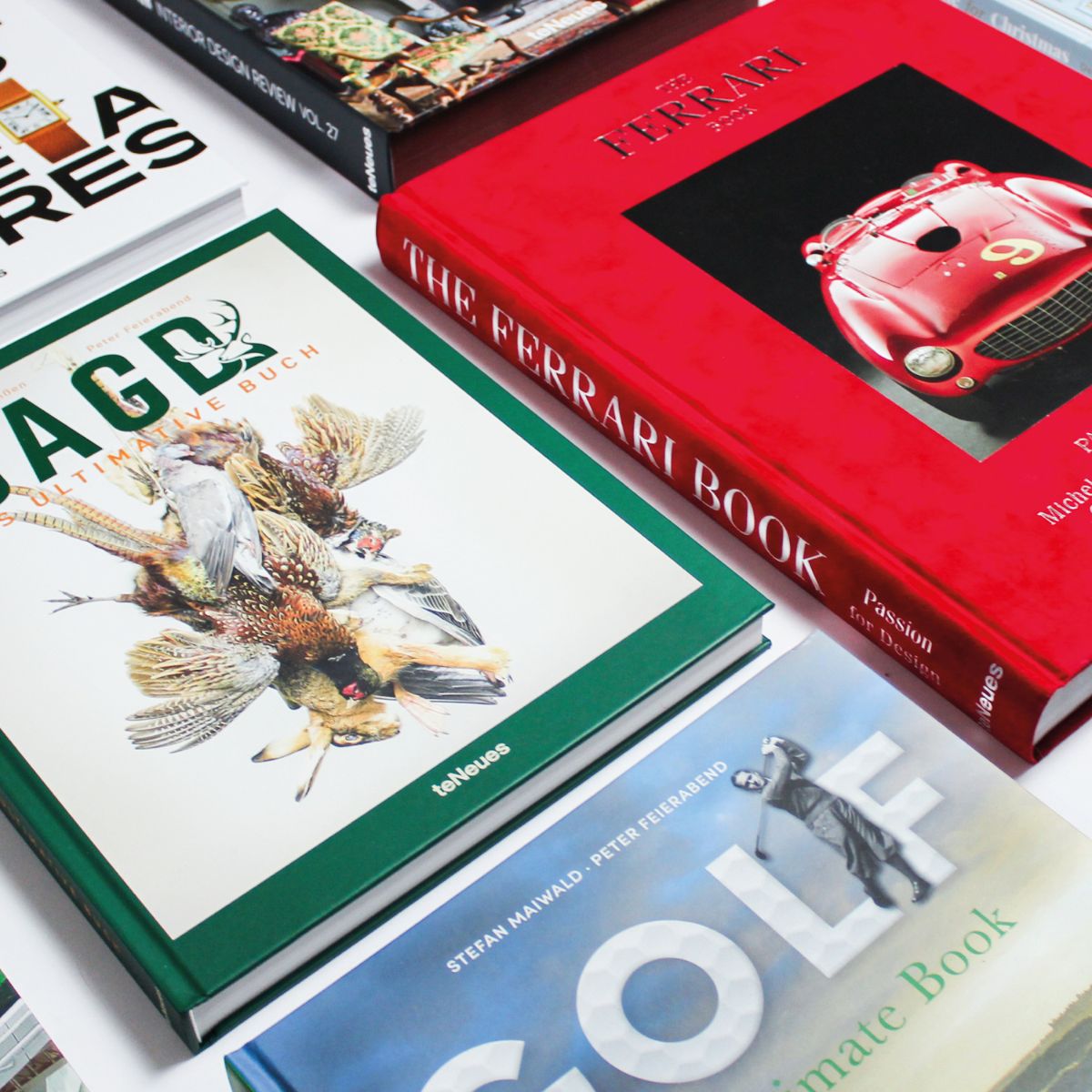 Stack of books including 'The Ferrari Book' and 'Golf: The Ultimate Book' on a white surface.