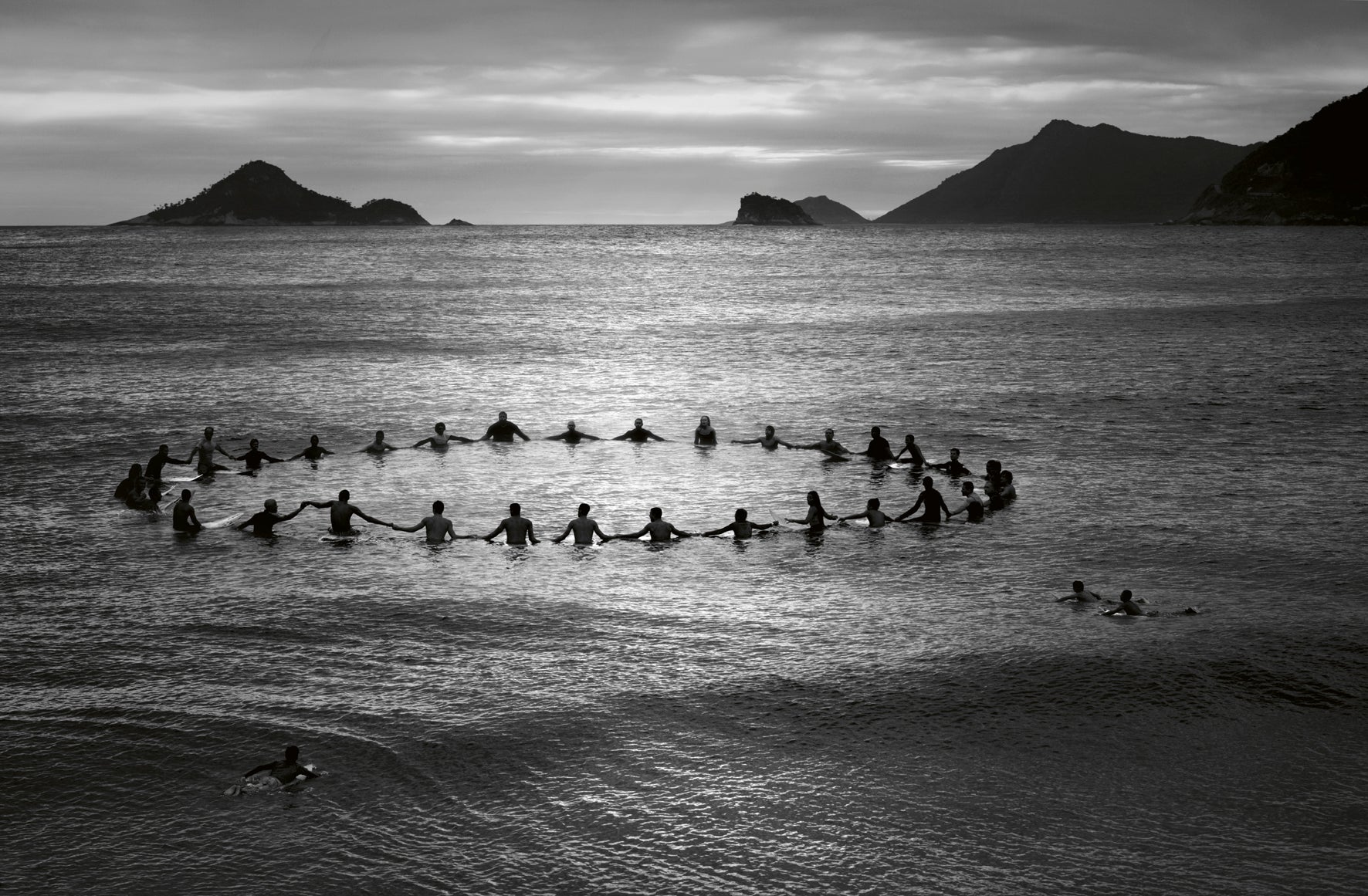 Group of surfers forming a circle in the ocean with mountains in the background