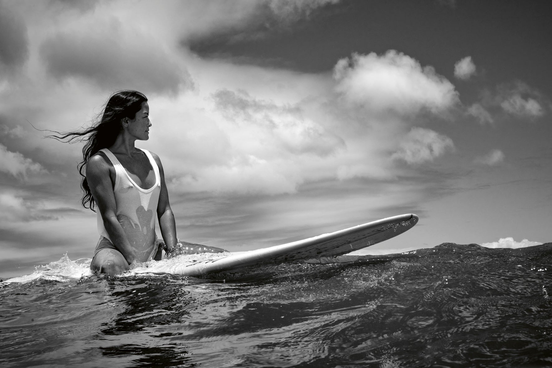 Person holding a surfboard in the ocean with a cloudy sky.
