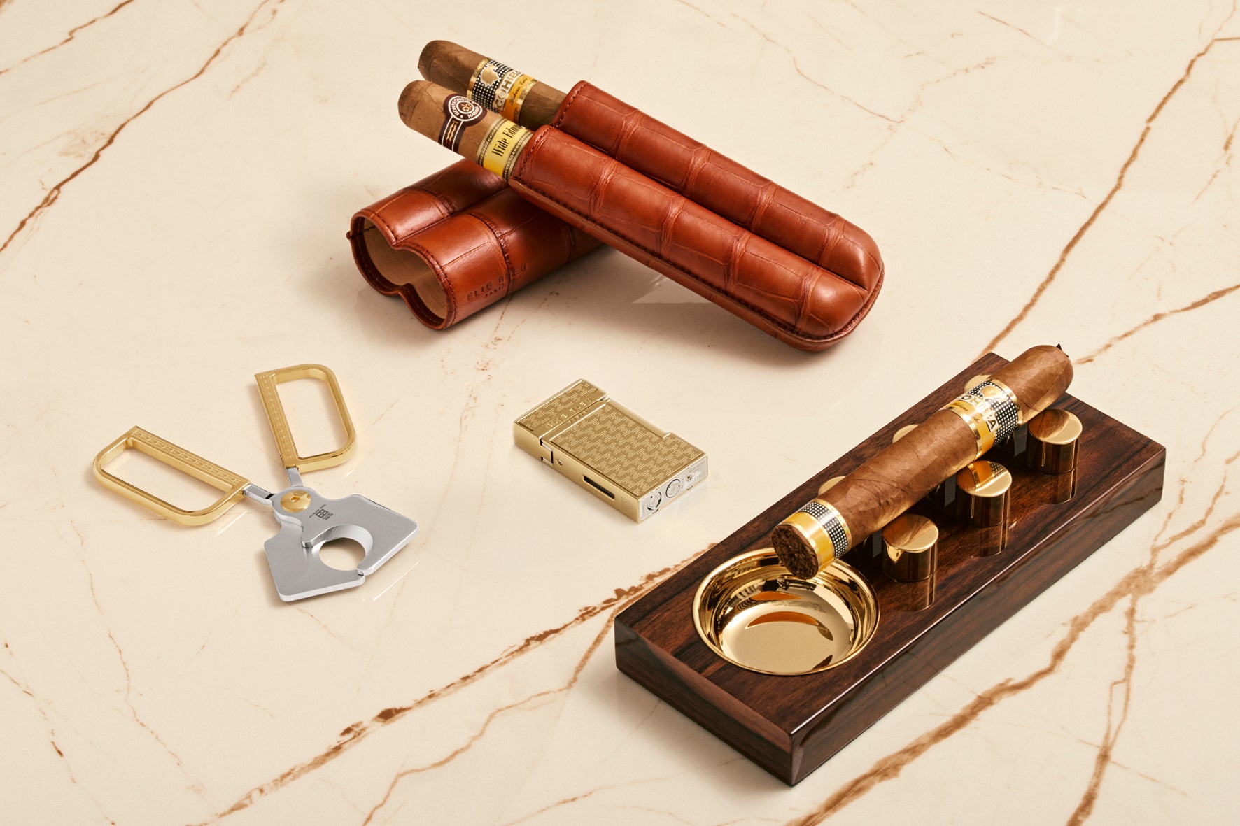 Cigar accessories including a humidor, cutter, and lighter on a marble surface
