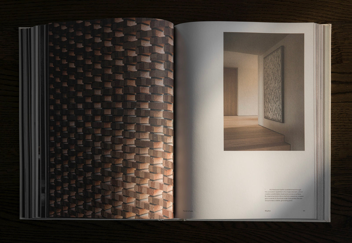 An open architectural design book displayed flat on a dark wooden surface, showing a detailed photograph of textured brown and beige tiles on the left page and an interior hallway scene on the right page.