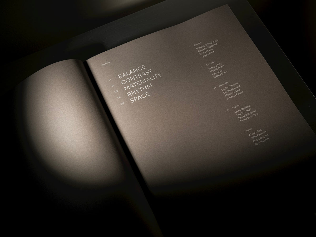 An open dark gray booklet or booklet on a black background, with a spotlight illuminating one page that reads 'BALANCE CONTRAST MATERIALITY RHYTHM SPACE'.