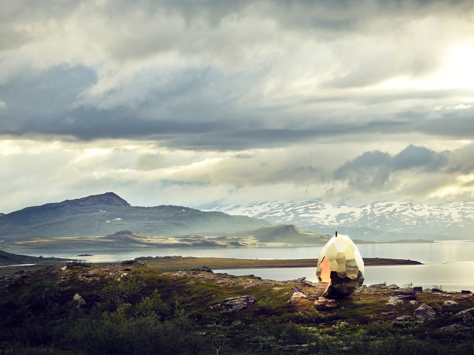 Tent pitched on a grassy hill with a scenic view of mountains and water under a cloudy sky.