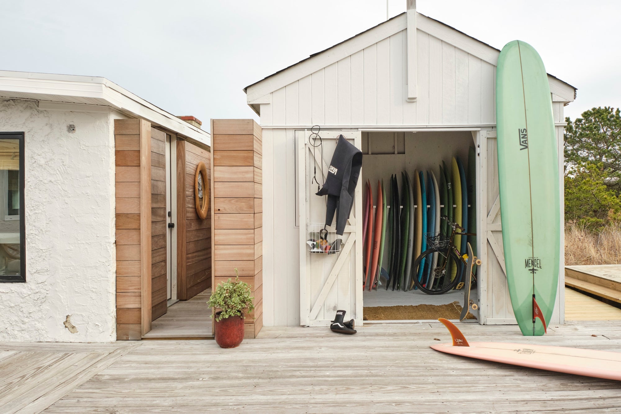 White shed with surfboards inside and on the exterior, near a wooden deck.