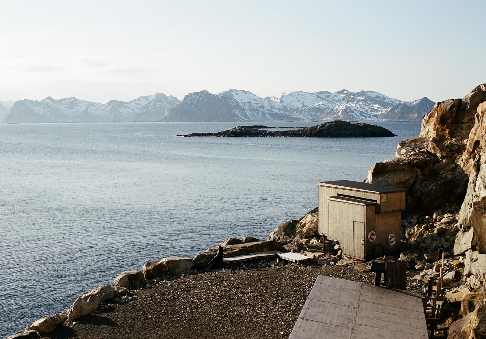 Rustic cabin by a body of water with snow-capped mountains in the background