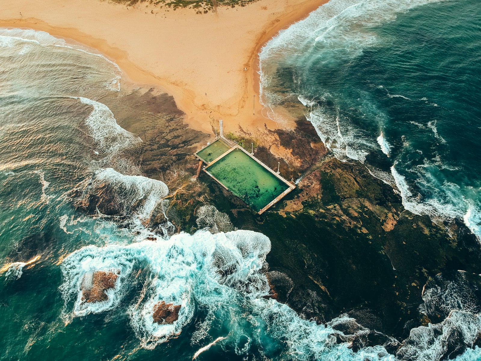 A natural pool surrounded by ocean waves and rocky shoreline.