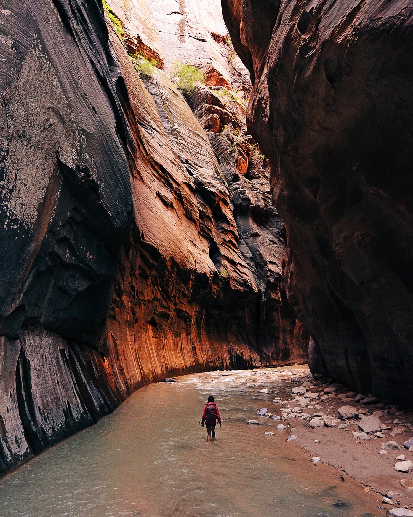 Person hiking through a narrow canyon with towering rock walls.