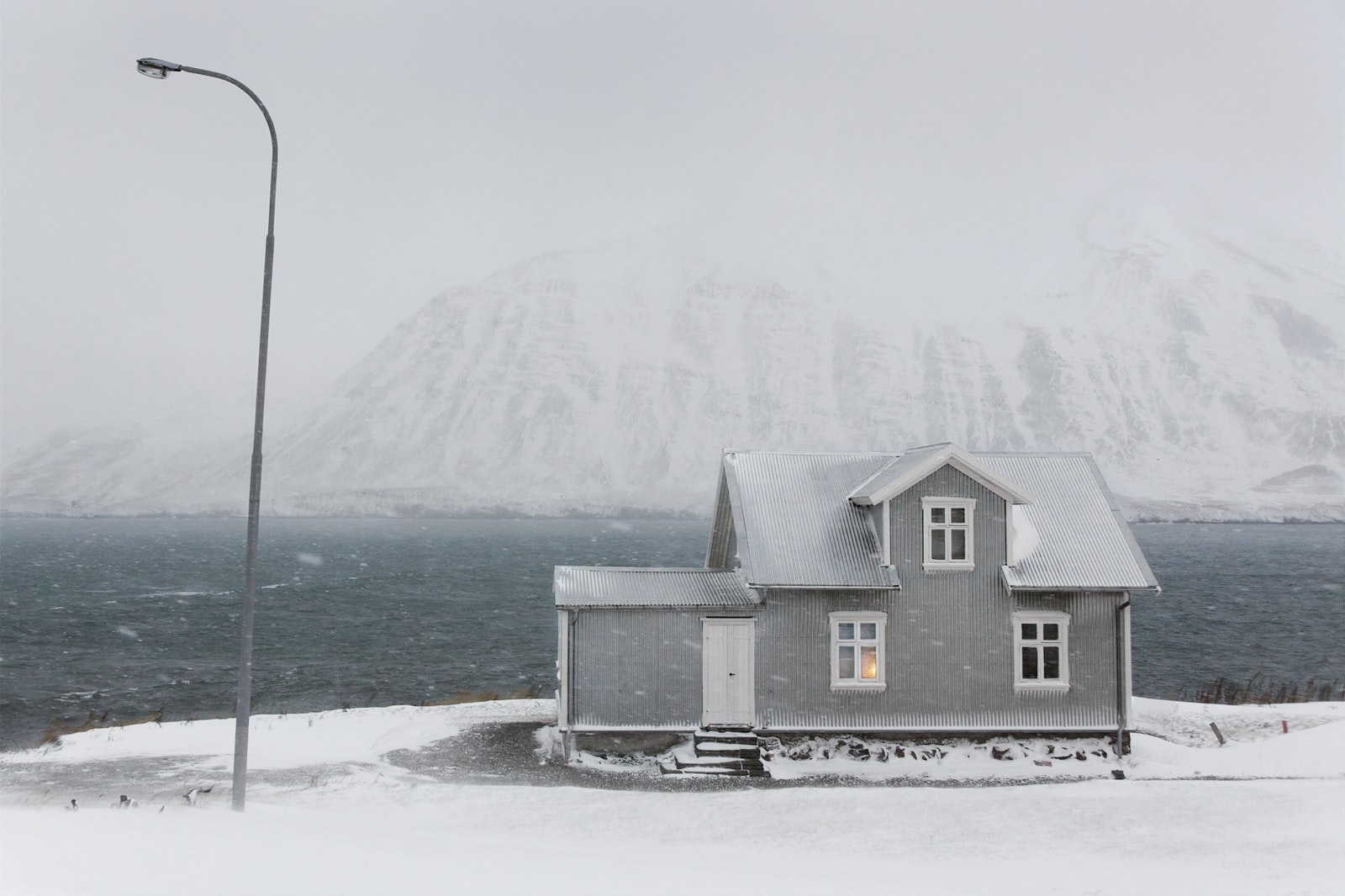 Small house by a body of water with snow-covered mountains in the background