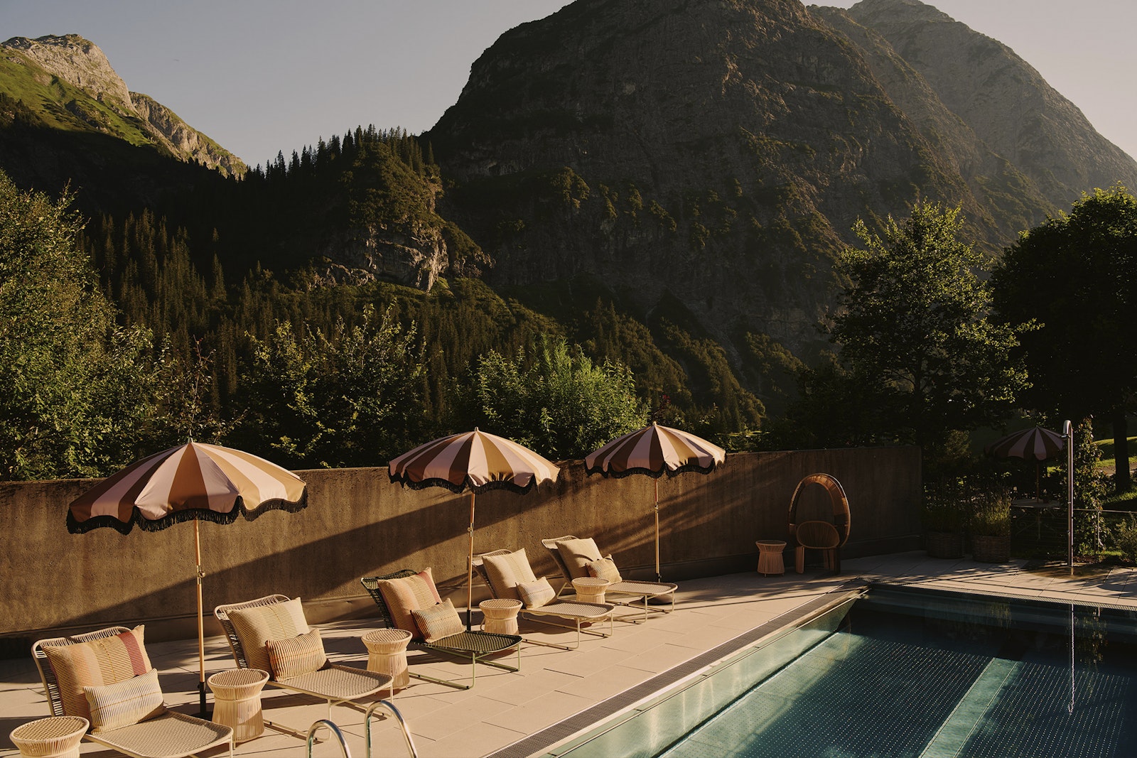 Outdoor pool area with lounge chairs and umbrellas against a mountainous backdrop