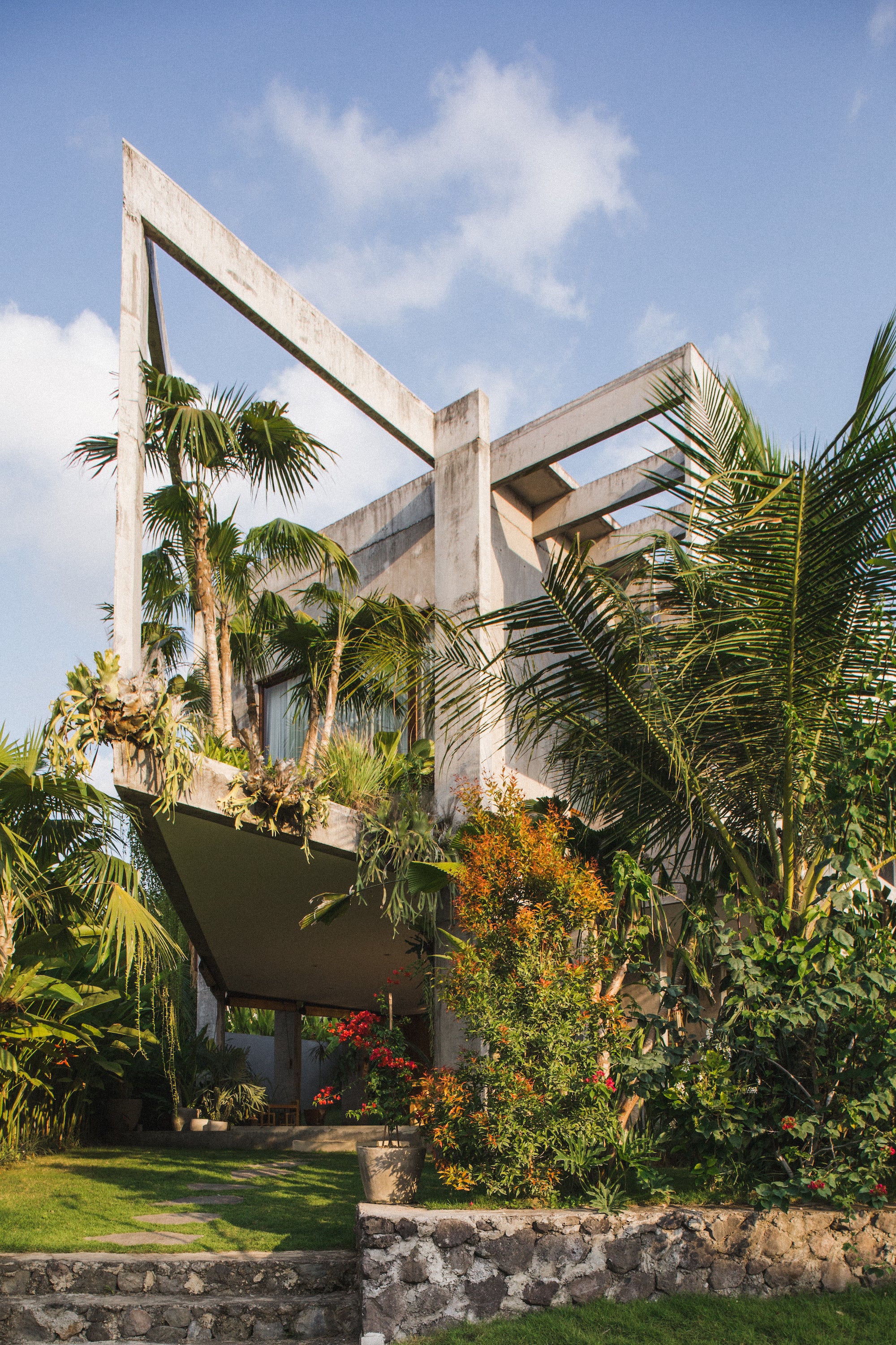 Located in a small valley on Bali’s southern coast, this geometric concrete home was designed as a collaboration between architectural studio Patisandhika and multidisciplinary designer Daniel Mitchell. Inspired by the American architect Ray Kappe, the L-shaped structure blurs the divide between the indoors and outdoors. It creates a series of changing moods  through a dynamic layout and material selection.